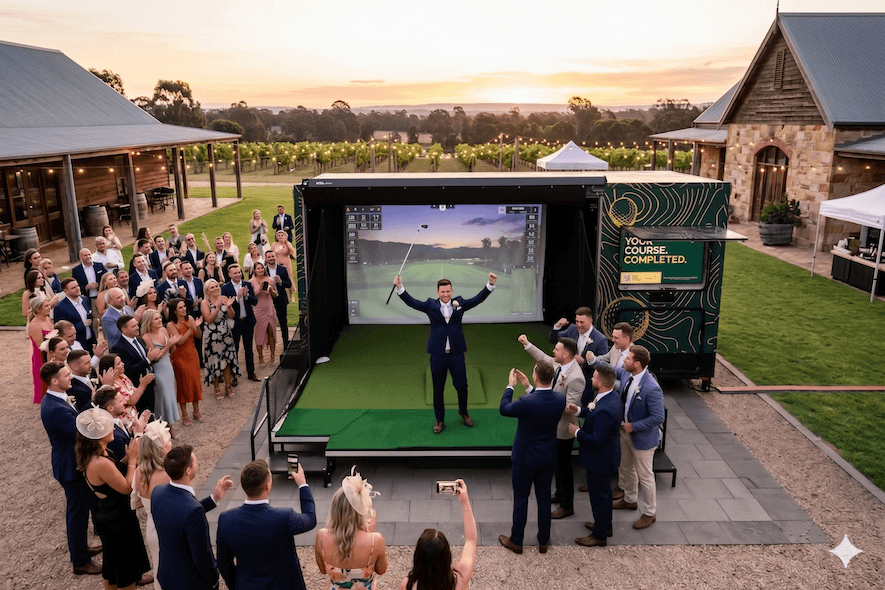 Wedding guests in formal attire watching a groomsman play the Golf Daze simulator during cocktail hour at a vineyard